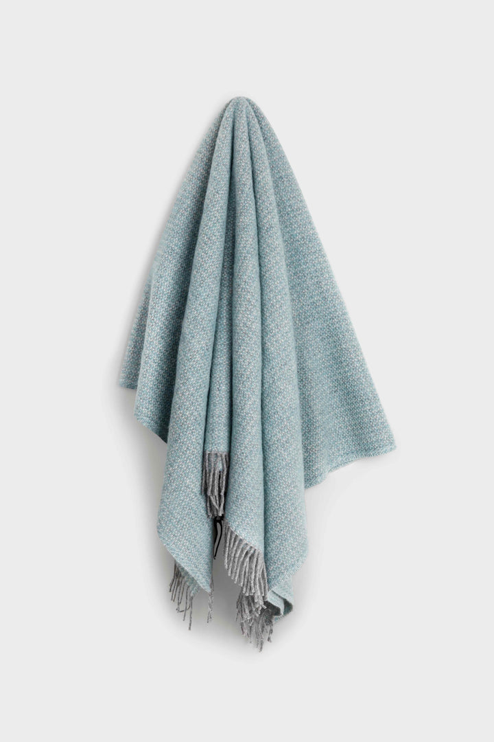 Belle & Aube Bamford Wool blanket in Seafoam hanging on a wall hook, showcasing elegant drape and fine weave